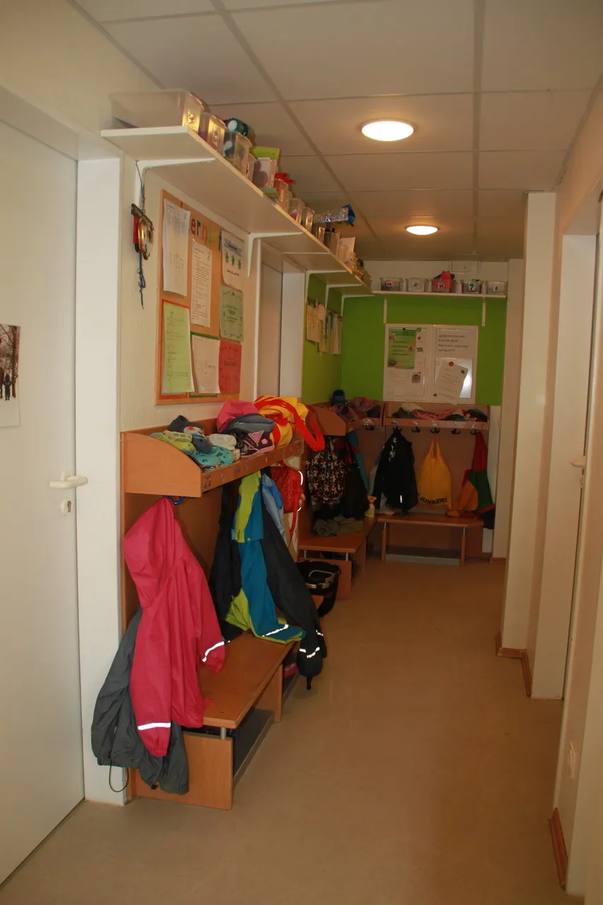Garderobe mit Kinderjacken an Haken und einer Sitzbank davor.