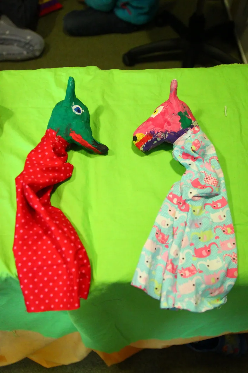 Zwei selbst genähte Handpuppen mit Pferdeköpfen liegen auf einem grünen Tuch.