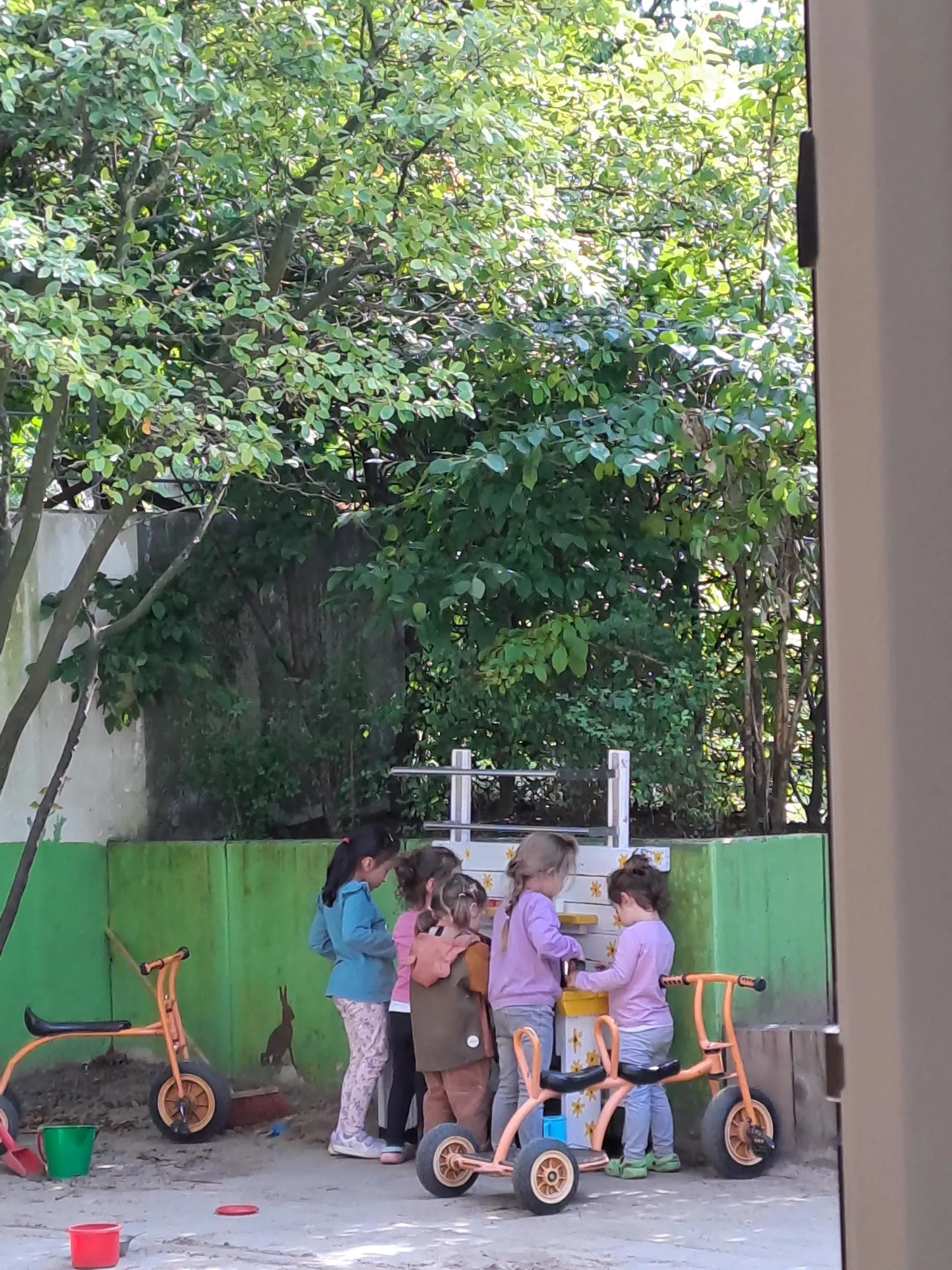 Blick aus dem Kinderladen nach draußen; im Hintergrund stehen Kinder an der neuen Matschküche.