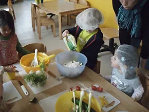 Drei Kinder schneiden und rühren gemeinsam an einem Tisch.