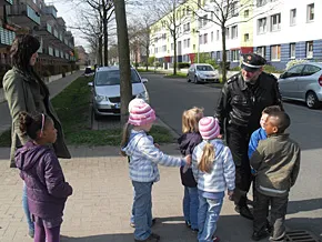 Eine Gruppe Kinder überquert gemeinsam mit einem Polizisten eine Straße.